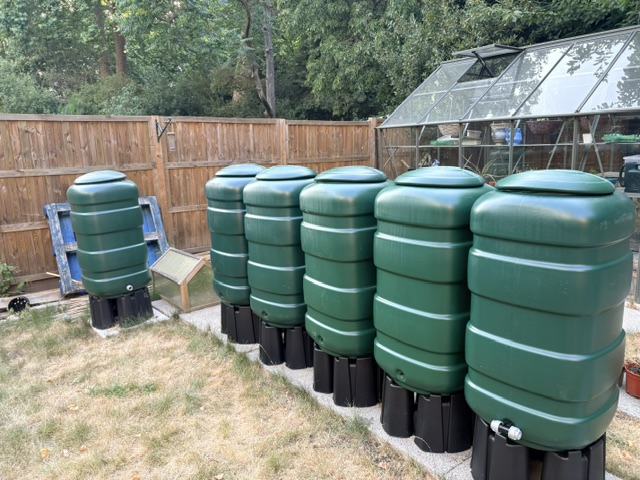 Row of rainwater harvesting butts installed along a fence line